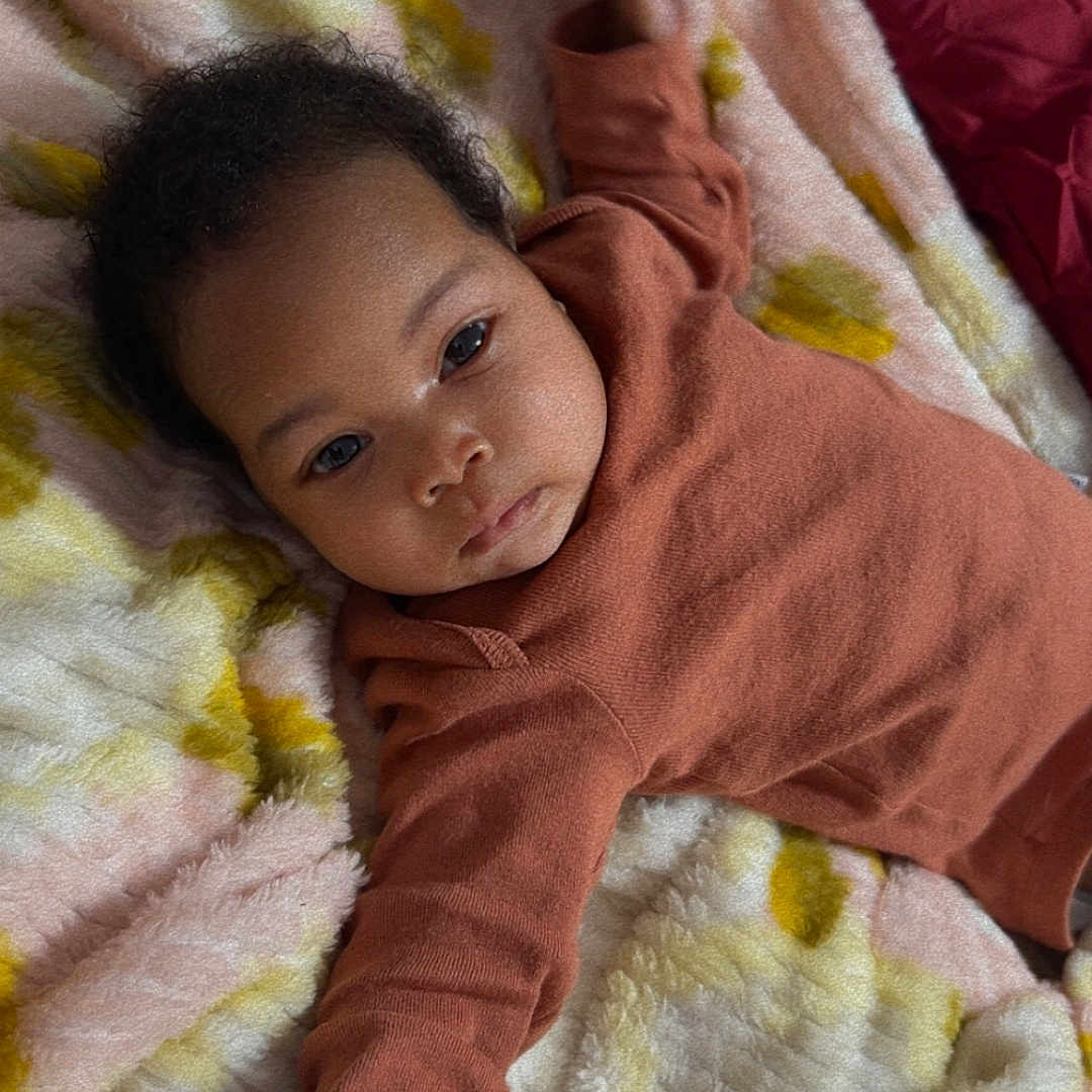 Xailia is registered to the contest to win money with this photo: arm, baby, blanket, child, cozy, curly_hair, cute, fabric, face, hand, indoor, infant, lying_down, onesie, pastel_colors, resting, soft, texture, toddler, warm