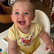 Olive-Marie joined the competition — help win amazing prizes! baby, child, smiling, high_chair, yellow_dress, blue_eyes, indoor, happy, cute, toddler, cartoon_print, toy, hair_bow, skin, face, hand, furniture, room, floor, person
