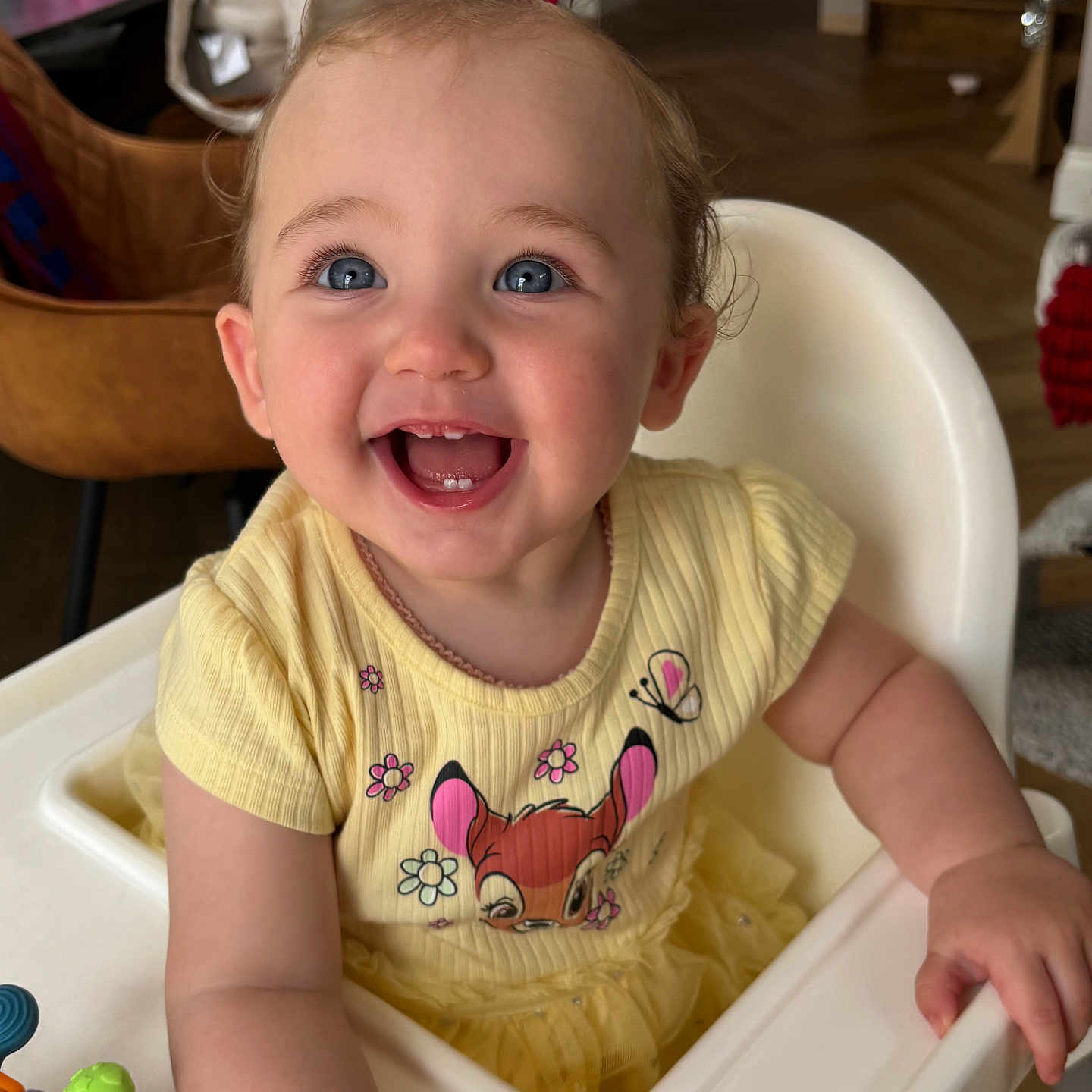 Olive-Marie joined the competition — help win amazing prizes! baby, blue_eyes, cartoon_print, child, cute, face, floor, furniture, hair_bow, hand, happy, high_chair, indoor, person, room, skin, smiling, toddler, toy, yellow_dress