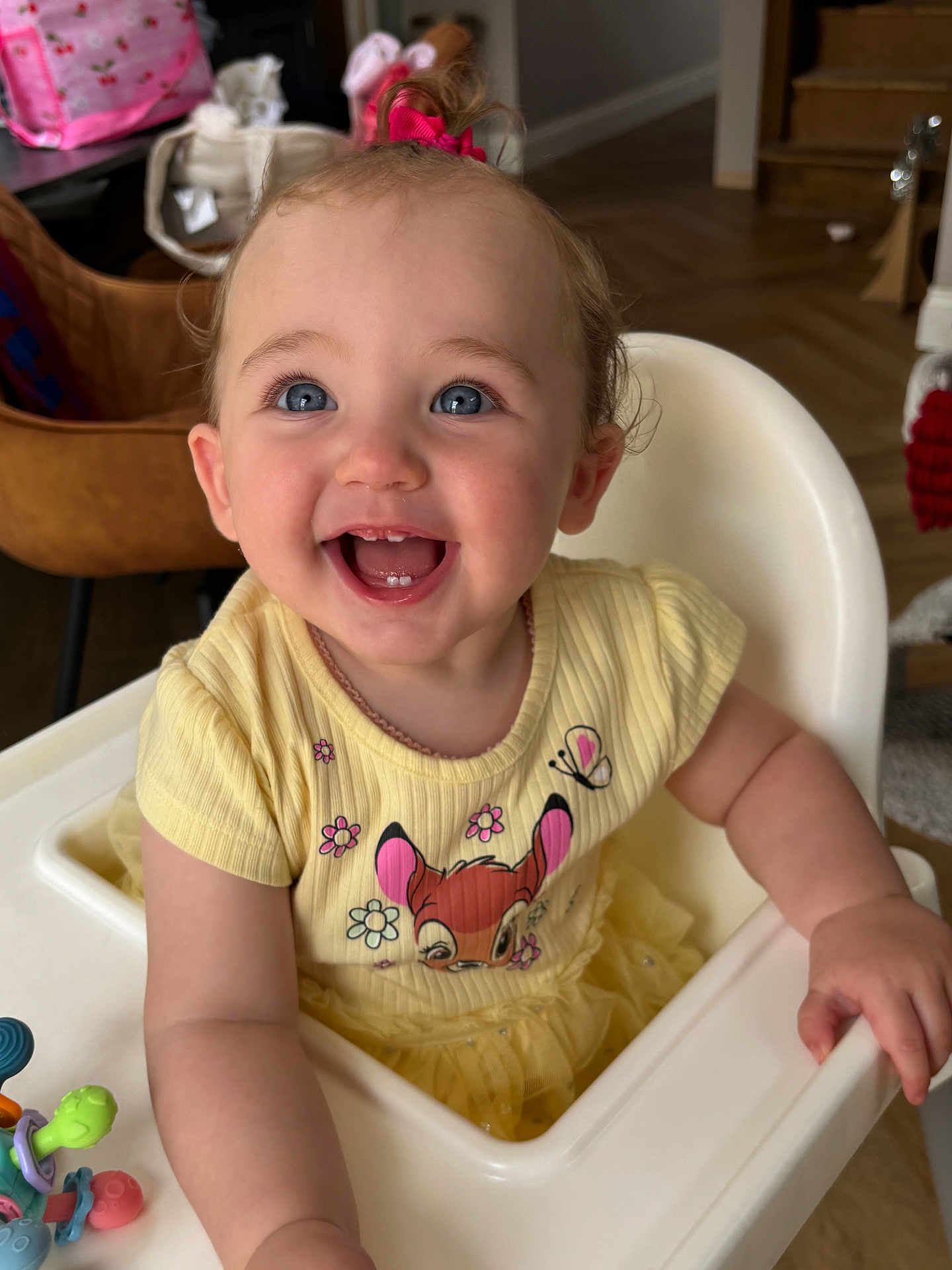 Olive-Marie joined the competition — help win amazing prizes! baby, child, smiling, high_chair, yellow_dress, blue_eyes, indoor, happy, cute, toddler, cartoon_print, toy, hair_bow, skin, face, hand, furniture, room, floor, person