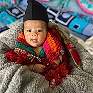 Shriyan joined the competition — help win amazing prizes! baby, infant, child, knitted_scarf, colorful_clothing, black_hat, blanket, cozy, face, expression, tongue_out, hand, foot, decorative_dagger, indoor, portrait, cute, soft_texture, patterned_background, wrapped