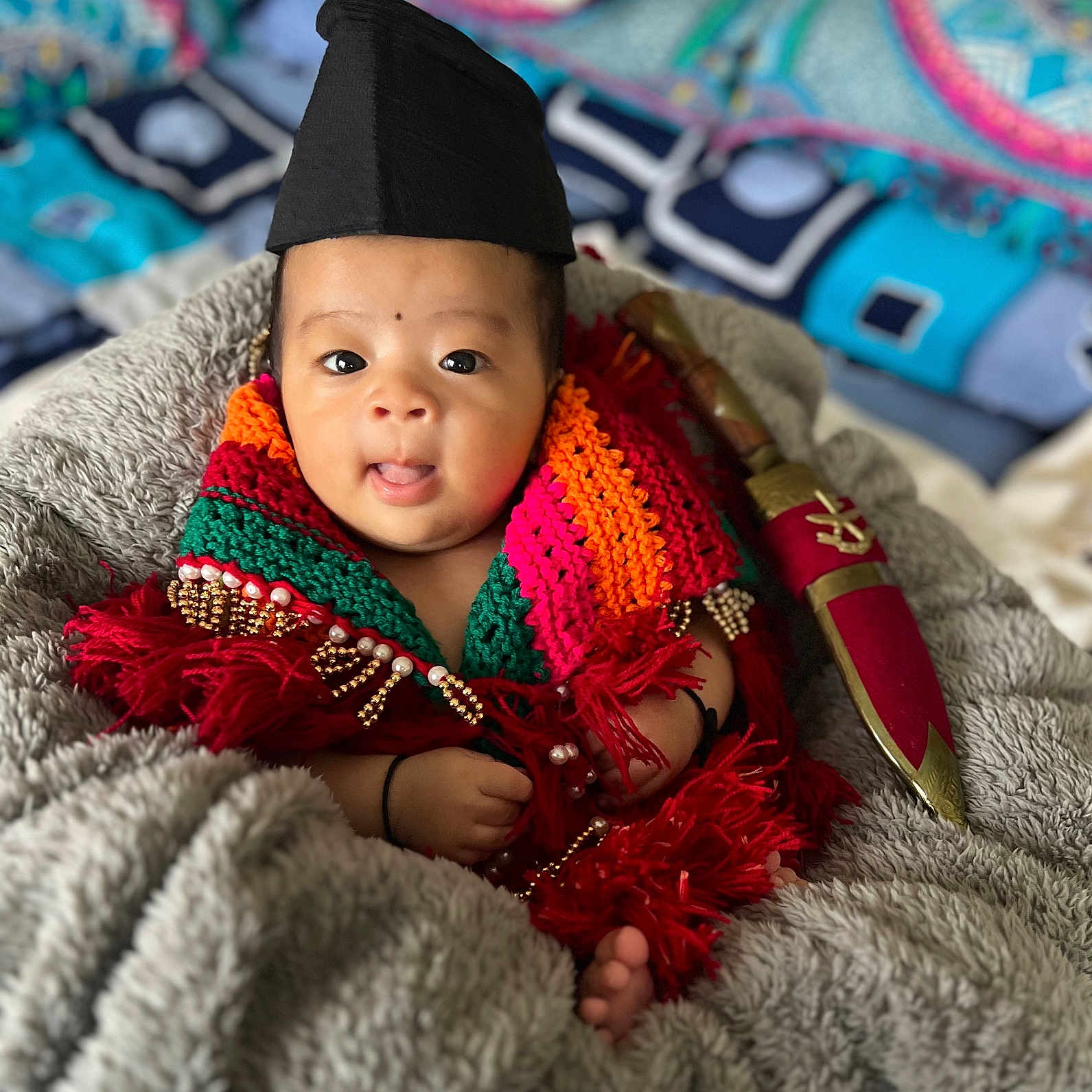 Shriyan joined the competition — help win amazing prizes! baby, black_hat, blanket, child, colorful_clothing, cozy, cute, decorative_dagger, expression, face, foot, hand, indoor, infant, knitted_scarf, patterned_background, portrait, soft_texture, tongue_out, wrapped