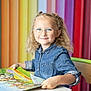 bright_colors, chair, child, colorful_background, curly_hair, denim_shirt, early_learning, education, girl, glasses, happy, indoors, kid, picture_book, portrait, preschool, rainbow, reading, sitting, smiling