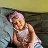 baby, child, infant, smile, headband, pink_bow, colorful_clothing, couch, gray_blanket, relaxed, indoors, portrait, cute, happy, young_child, seated, skin, face, hands, eyes
