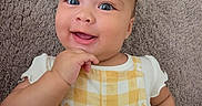 Amina is registered to the contest to win money with this photo: baby, carpet, checkered, child, cute, eyes, face, hand, happy, indoors, infant, person, portrait, sitting, skin, smiling, texture, white_shirt, yellow_outfit, young_child