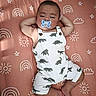 baby, sleeping, pacifier, dinosaur_print, romper, blanket, pattern, sun, cloud, star, rainbow, infant, cute, relaxed, child, indoors, soft_lighting, portrait, laying_down, peaceful