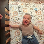 Elijah is registered to the contest to win money with this photo: baby, crib, bedding, animal_print, smiling, happy, infant, child, cute, playful, giraffe, elephant, lion, rainbow, stars, clouds, pajamas, blue_pants, beige_shirt, indoor