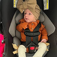 Ava is registered to the contest to win money with this photo: baby, car_seat, child, infant, hat, bow, orange_clothing, straps, seatbelt, legs, white_socks, ribbons, cute, indoor, safety, young_child, person, portrait, newborn, cozy