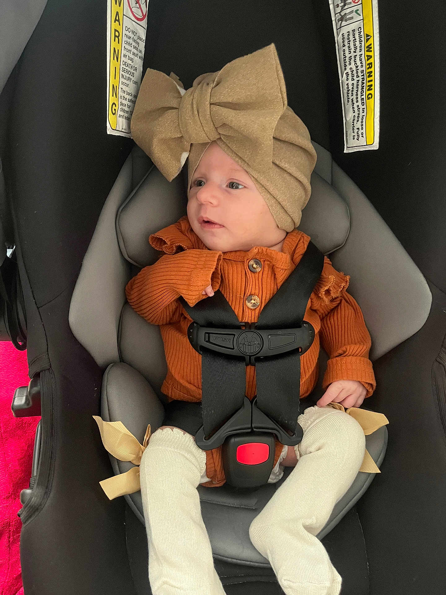 Ava is registered to the contest to win money with this photo: baby, car_seat, child, infant, hat, bow, orange_clothing, straps, seatbelt, legs, white_socks, ribbons, cute, indoor, safety, young_child, person, portrait, newborn, cozy