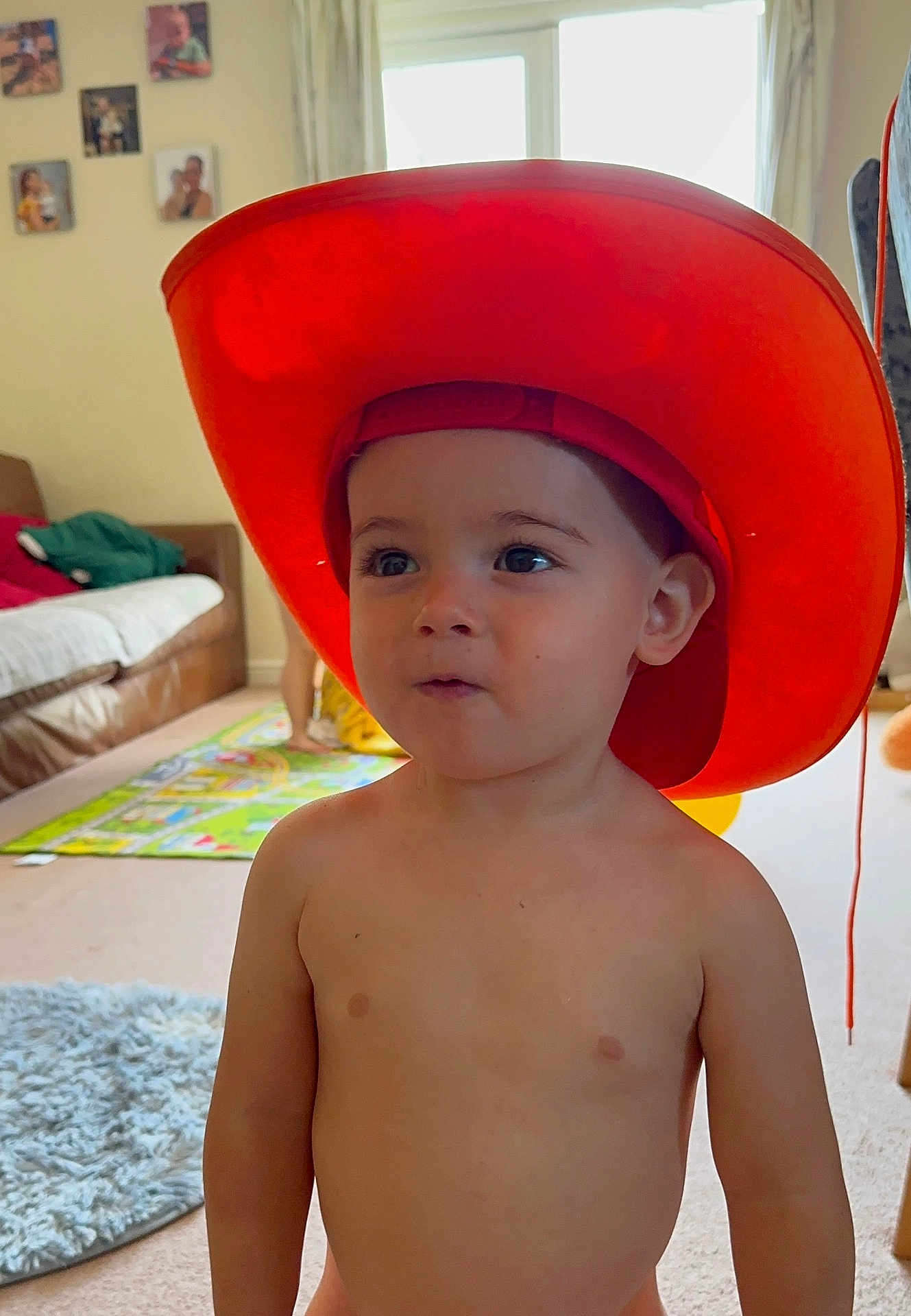 Tudor joined the competition — help win amazing prizes! toddler, child, hat, orange, indoor, living_room, carpet, rug, shirtless, curious, portrait, person, family_photos, window, furniture, couch, home, young_child, expression, bright