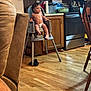 toddler, child, high_chair, diaper, kitchen, wooden_cabinets, stainless_steel_appliance, floor, tattoo, arm, chair, paper_towel, pot, pan, countertop, table, wooden_floor, person, indoor, home