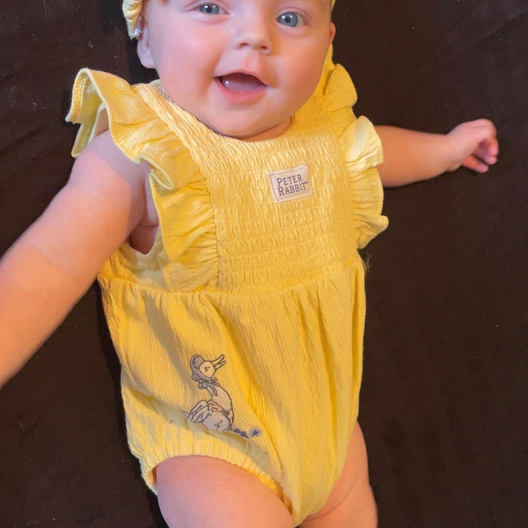 Skyla is registered to the contest to win money with this photo: accessories, baby, bodypart, bonnet, cap, clothing, costume, dress, face, finger, hand, hat, head, newborn, person, photography, portrait, sitting, sunhat, wood