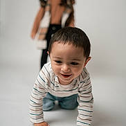 Ezekiel joined the competition — help win amazing prizes! child, toddler, baby, sibling, crawling, portrait, studio, smile, striped_shirt, jeans, hands, face, hair, background_blur, depth_of_field, indoor, playful, white_backdrop, standing_child, closeup