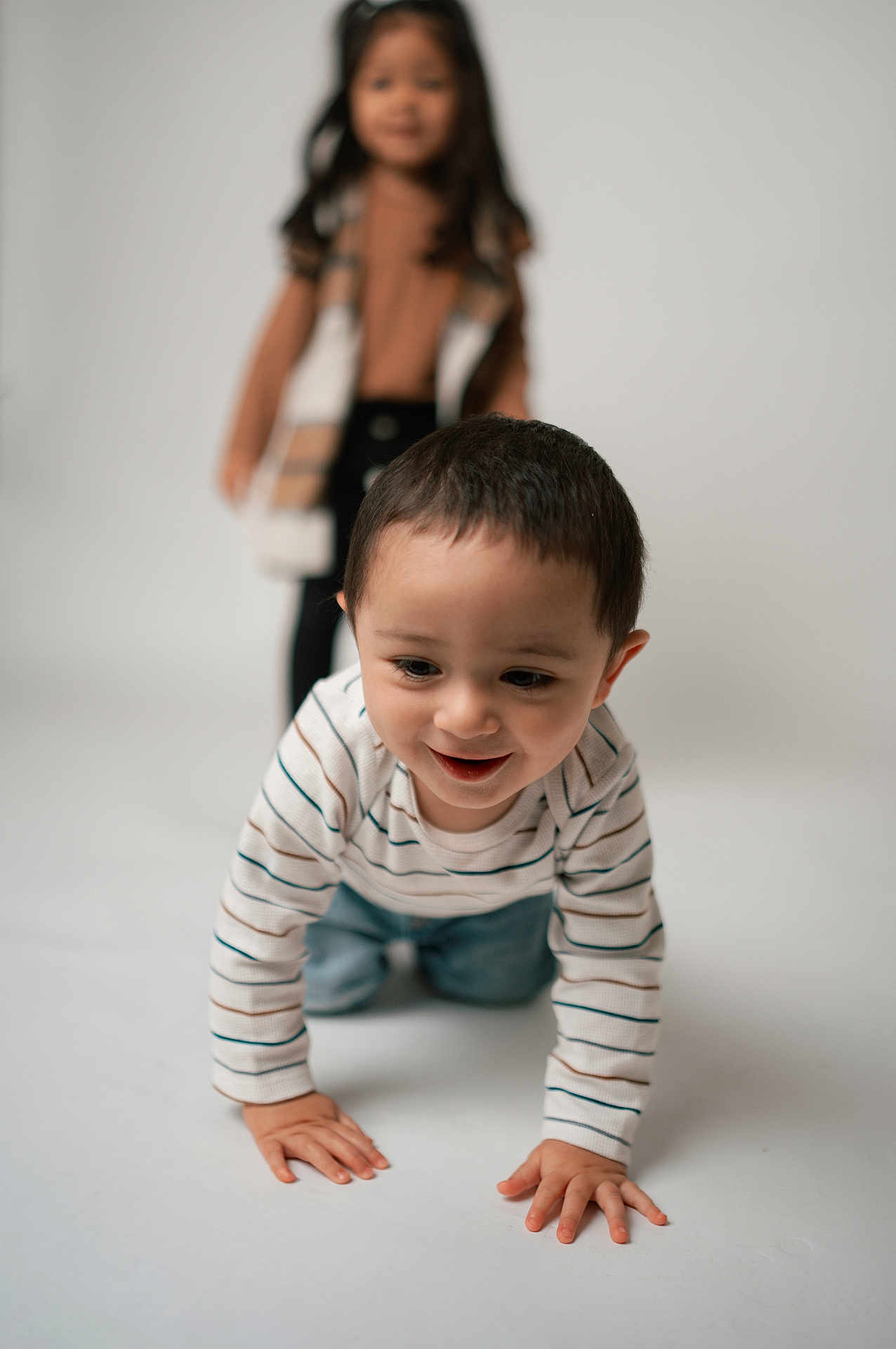 Ezekiel joined the competition — help win amazing prizes! child, toddler, baby, sibling, crawling, portrait, studio, smile, striped_shirt, jeans, hands, face, hair, background_blur, depth_of_field, indoor, playful, white_backdrop, standing_child, closeup