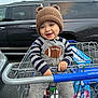 Ezekiel is registered to the contest to win money with this photo: child, toddler, shopping_cart, parking_lot, knit_hat, hat_with_ears, smiling, onesie, striped_sleeves, football_patch, hands, car, suv, blue_handle, grocery_store, seat, safety_belt, box_of_goods, gray_clothing, happy_face