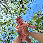 Olivia is registered to the contest to win money with this photo: baby, child, person, hands, tree, sky, blue_sky, green_leaves, outdoor, nature, smiling, cute, infant, arms, holding, sunlight, daylight, happy, portrait, baby_clothing