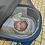 baby, stroller, hoodie, mesh_screen, outdoor, child, face, wheel, pavement, clothing, blanket, cute, infant, person, transport, warm, walking, footpath, casual, small