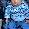 baby, child, car_seat, blue_hat, knitwear, sweater, patterned_clothing, blue_pants, socks, infant, portrait, serious_expression, indoors, seatbelt, cute, young_child, clothing, person, closeup, casual