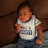 baby, infant, bib, clothing, denim_jeans, striped_shirt, blanket, couch, indoor, person, child, face, sitting, footwear, cute, young, expression, soft_texture, relaxed, casual