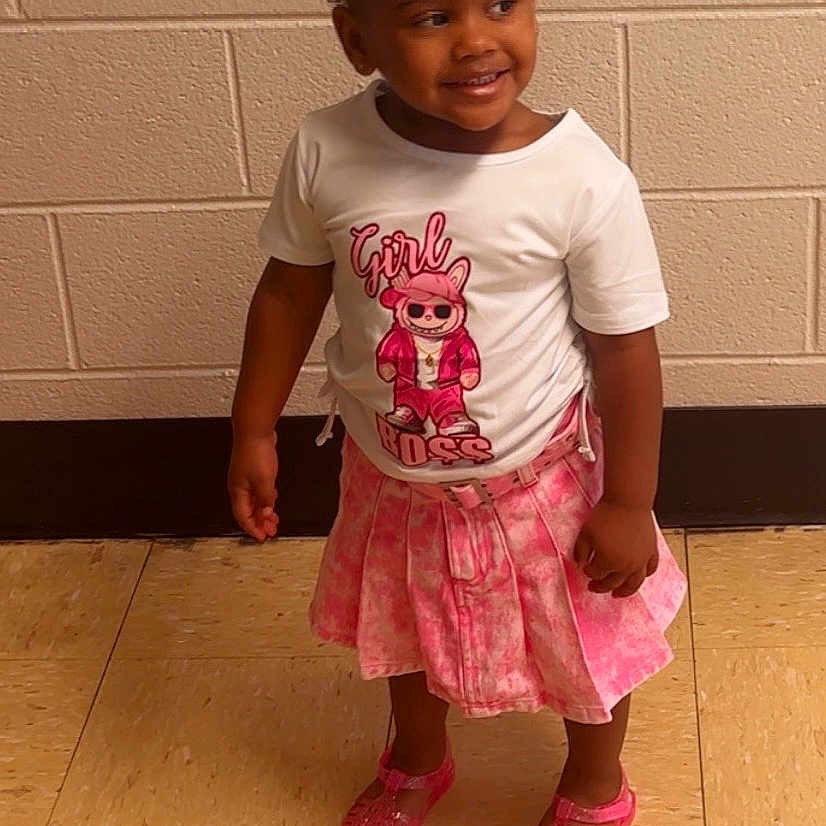 Rhyani joined the competition — help win amazing prizes! toddler, girl, child, smiling, standing, pink_skirt, white_tshirt, pigtails, beads, indoor, tile_floor, brick_wall, shoes, happy, cute, fashion, portrait, person, young_child, casual_clothing