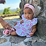 baby, child, girl, headband, pink, dress, outdoor, stone_wall, sandal, hand, helping_hand, curious, expression, sitting, portrait, footwear, nature, blurred_background, person, cute