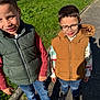 Emilio participe au concours pour gagner de l'argent avec cette photo : child, boy, glasses, green_vest, brown_vest, jeans, sneakers, outdoor, grass, sidewalk, sunlight, shadow, smile, casual_clothing, hooded_vest, happy, two_children, daylight, nature, playful