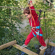Emilio participe au concours pour gagner de l'argent avec cette photo : activity, adventure, balance, boy, child, daylight, exploration, forest, glasses, harness, nature, outdoor, playground, red_clothing, rope_bridge, safety, trees, water, wooden_logs, young