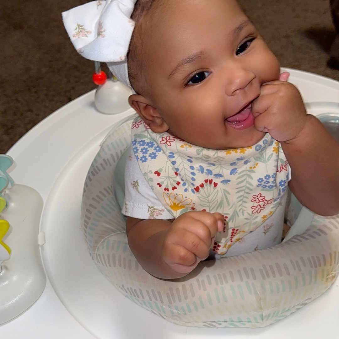 Aura is registered to the contest to win money with this photo: activity_center, baby, bow, carpet, chewing, child, clothing, cute, face, hands, happy, headband, indoor, infant, person, play, seat, smiling, toddler, toy