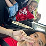 blue_eyes, car, casual_clothing, child, daylight, dinosaur_print, hand_gesture, interior, peace_sign, person, playful, portrait, red_shirt, seat, seatbelt, shorts, smile, white_shoes, window, young