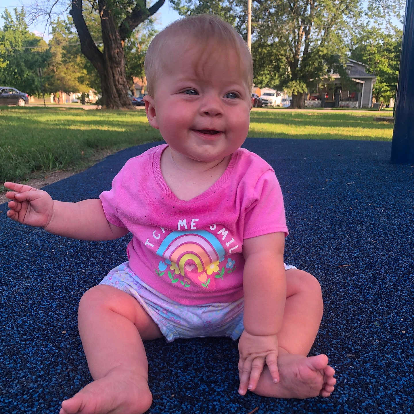 Saraina is registered to the contest to win money with this photo: baby, barefoot, child, cute, daytime, face, grass, happy, nature, outdoor, park, person, pink_shirt, playground, rainbow, shorts, sitting, smiling, sunlight, trees