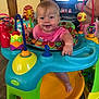 baby, child, activity_center, toys, indoor, smiling, happy, play, colorful, furniture, floor, television, person, clothing, feet, hand, face, room, wooden_floor, family