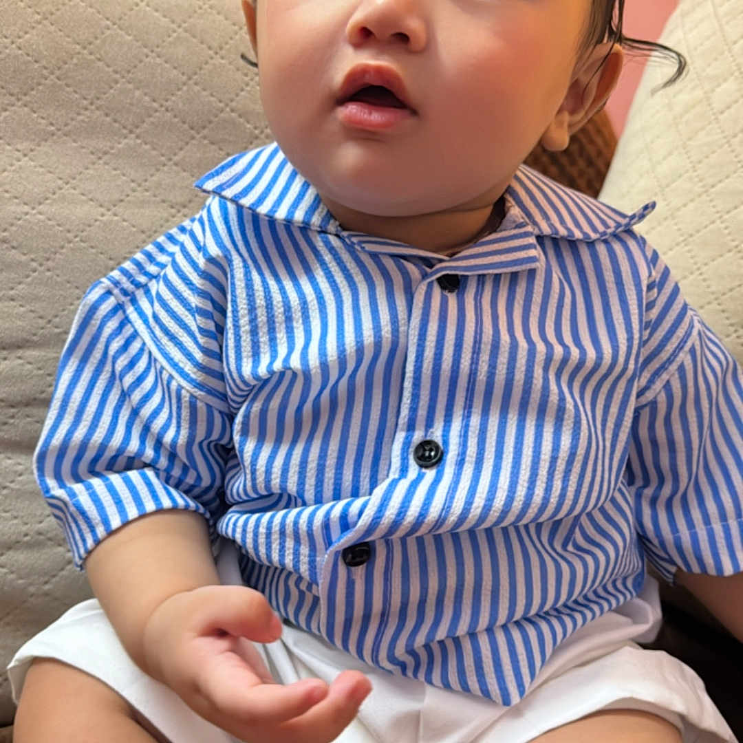 Manvay is registered to the contest to win money with this photo: baby, child, clothing, couch, curious, cute, expression, face, furniture, hair, hand, indoor, legs, person, portrait, sitting, skin, striped_shirt, white_shorts, young_child