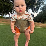 Elijah is registered to the contest to win money with this photo: baby, child, swing, playground, outdoor, greenery, grass, trees, infant, drool, cute, curious, park, summer, casual_clothing, shorts, striped_shirt, barefoot, daylight, nature
