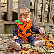 Matteo a rejoint le concours — aidez-le/la à gagner de superbes lots ! autumn_leaves, baby_shoes, casual_clothing, child, costume, curious, cute, fall, leaf, nature, outdoor, playful, pumpkin_costume, seasonal, sitting, stone_pavement, stone_wall, toddler, wooden_fence, young_child