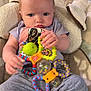 baby, child, toy, colorful_toy, blue_eyes, clothing, sitting, cushion, blanket, hand, face, indoor, infant, person, play, soft, comfort, cute, expression, young
