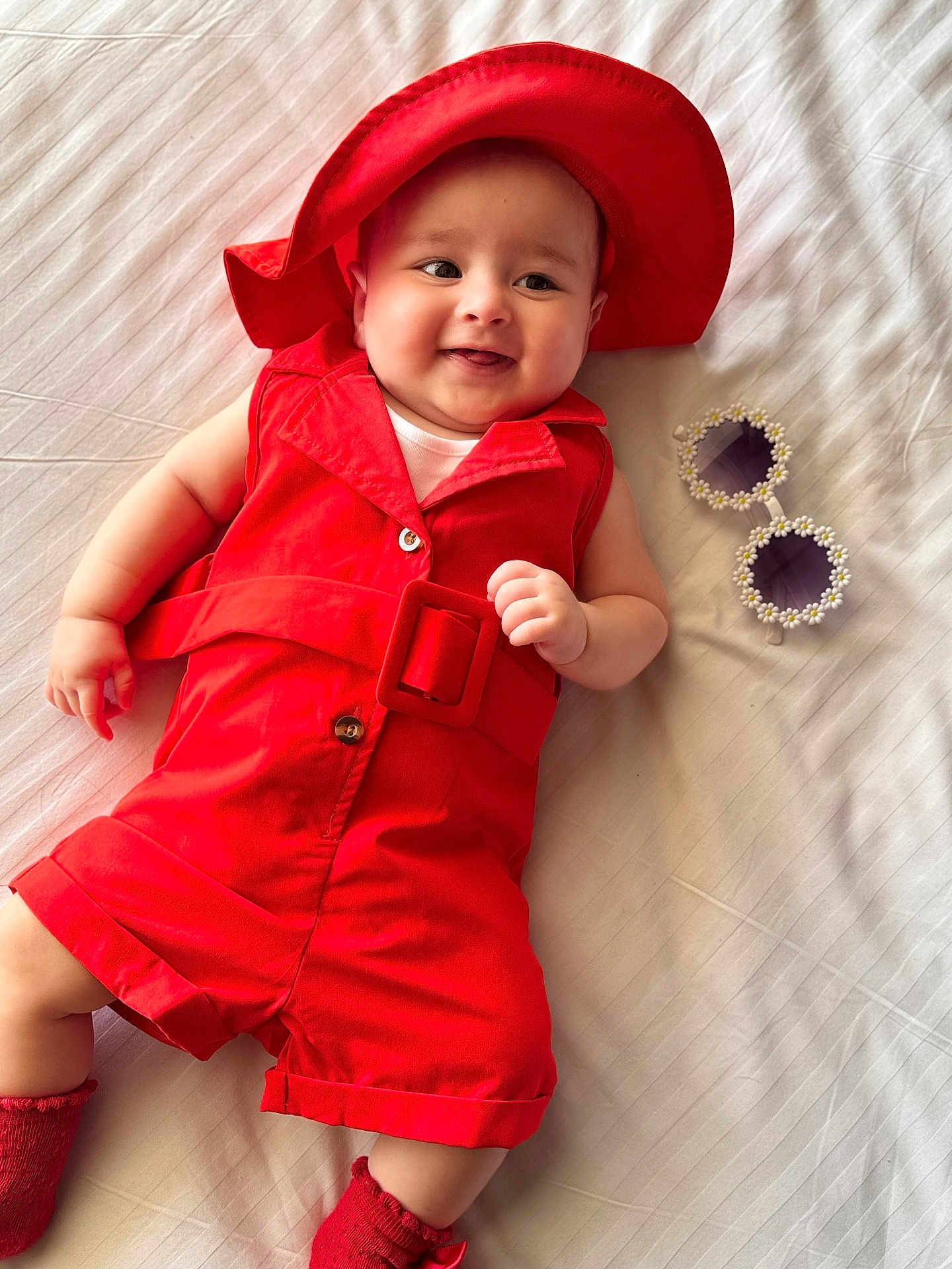 Lamaisah joined the competition — help win amazing prizes! baby, red_clothing, red_hat, smiling, lying_down, bed, white_bedspread, sunglasses, flower_frame, infant, cute, happy, child, indoor, portrait, footwear, sock, fashion, accessories, playful