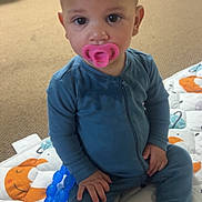 Destin is registered to the contest to win money with this photo: baby, pacifier, blue_onesie, teething_toy, play_mat, indoor, carpet, child, cute, sitting, infant, person, floor, toy, young_child, face, hands, feet, looking_at_camera, home