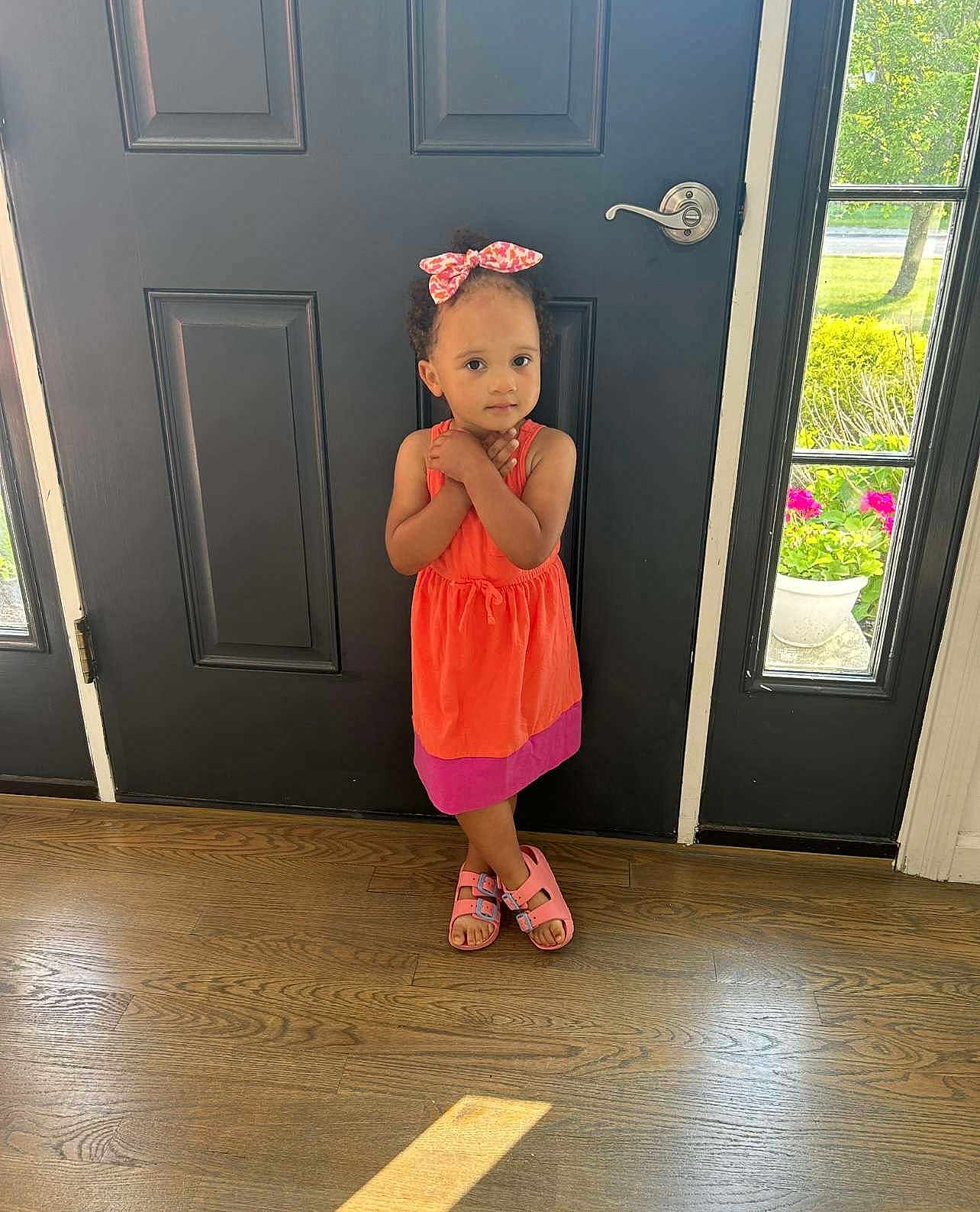 Ivory is registered to the contest to win money with this photo: child, girl, dress, standing, door, indoor, floor, wood_floor, sandals, hair_bow, curly_hair, portrait, person, cute, young_child, casual_clothing, natural_light, window, plant, shy