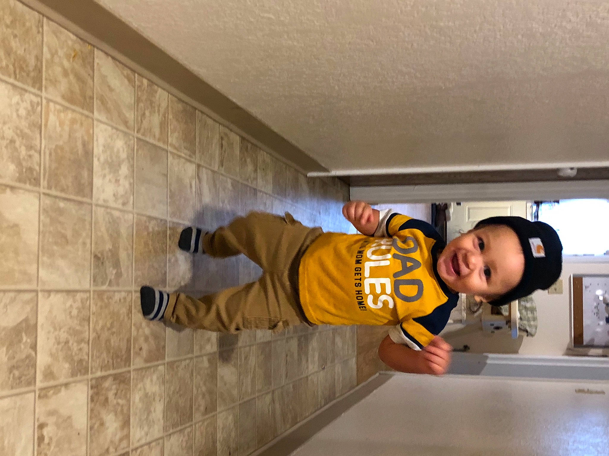 Alec is registered to the contest to win money with this photo: baby_toddler_clothing, child, cool, floor, flooring, headwear, outdoor_shoe, person, play, sock, standing, tile, tile_flooring, toddler, walking_shoe, wall