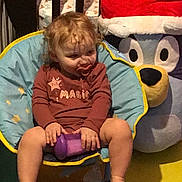 Eva joined the competition — help win amazing prizes! toddler, child, pacifier, purple_cup, curly_hair, blue_chair, yellow_trim, plush_bear, santa_hat, indoor, floor_mat, barefoot, clothing, happy, sitting, toy, holiday, cute, smile, baby