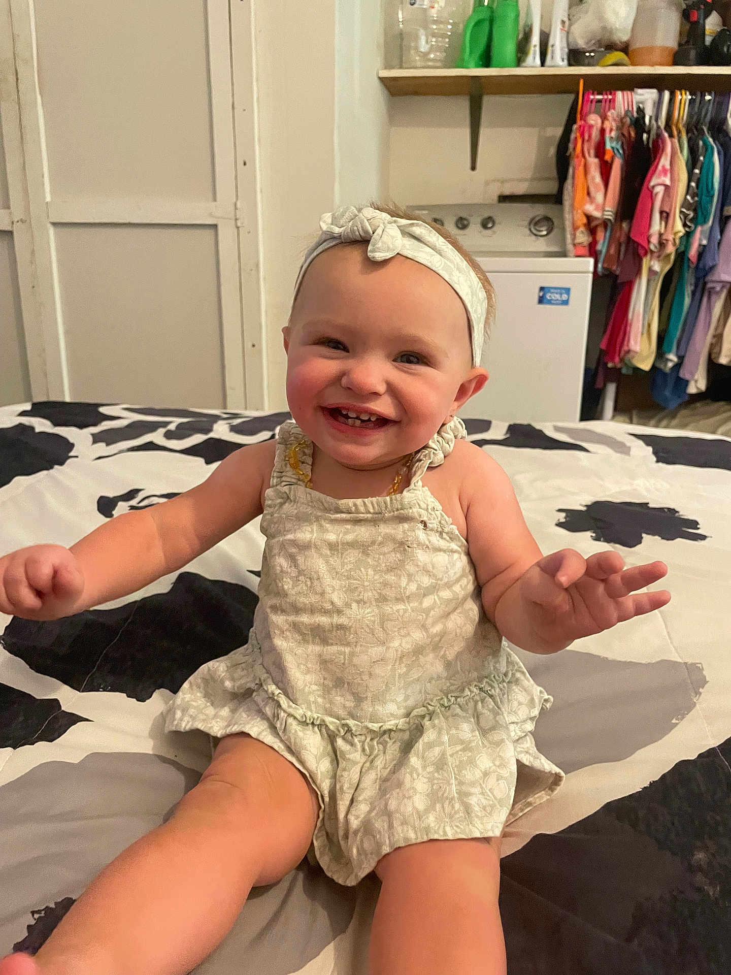 Oaklynn is registered to the contest to win money with this photo: baby, child, smiling, headband, dress, bed, blanket, indoor, furniture, clothing, happy, person, infant, young_child, cute, portrait, sitting, room, laundry, household