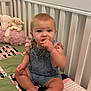 Oaklynn joined the competition — help win amazing prizes! baby, child, denim_overalls, crib, blanket, stuffed_animal, toy, nibble, sitting, indoor, cute, curious, pink, green, soft_toy, face, foot, hand, person, infant