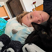 Binxs is registered to the contest to win money with this photo: cat, black_cat, person, face, eyes, cuddling, bedroom, bed, pillow, blanket, plush_toy, stuffed_animal, indoor, home, cozy, sleeping, lying_down, portrait, black_fur, green_eyes