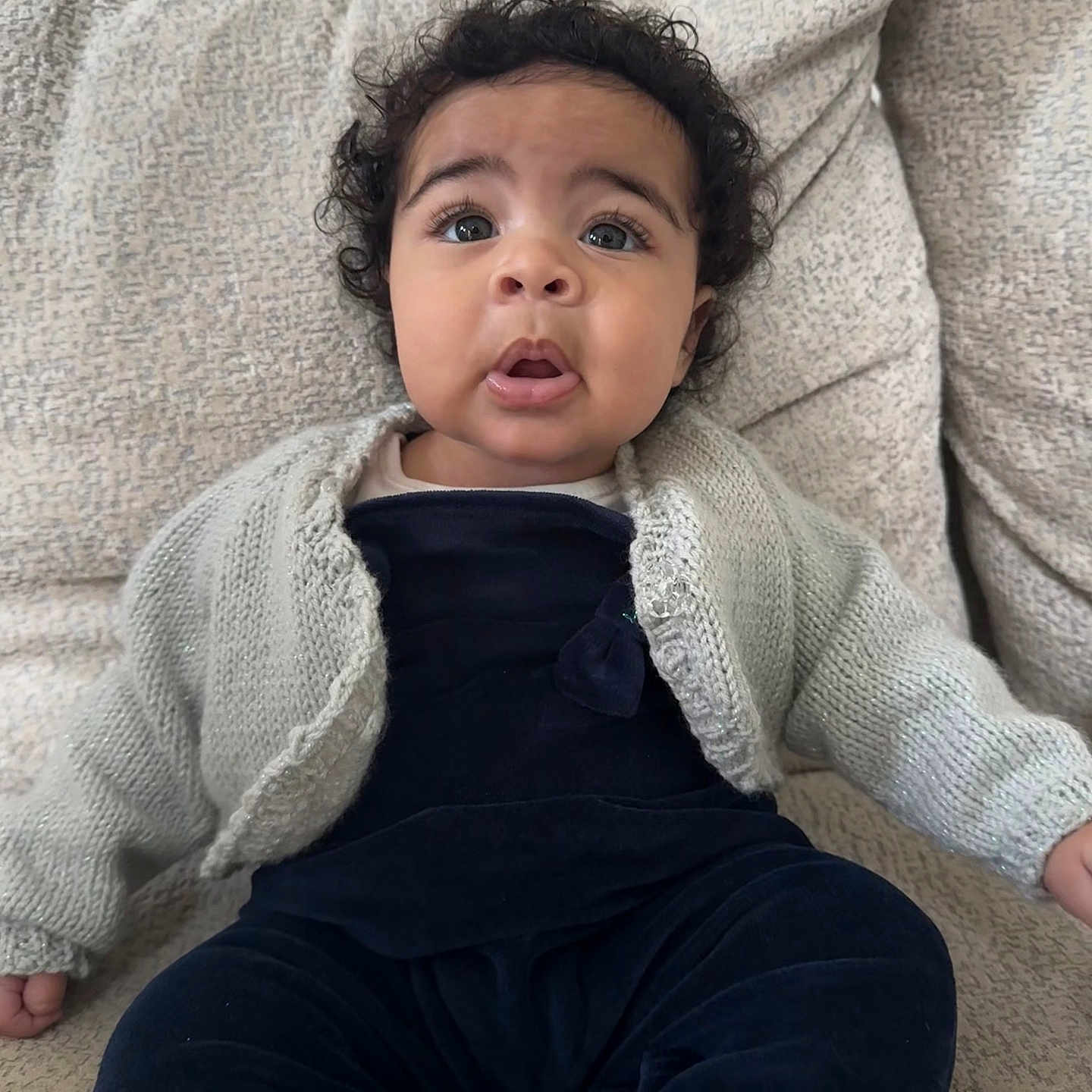 Nyah joined the competition — help win amazing prizes! baby, blue_eyes, casual_wear, child, couch, cozy, curly_hair, cute, expression, furniture, home, indoor, infant, knitted_cardigan, person, portrait, sitting, soft_texture, velvet_clothing, young_child