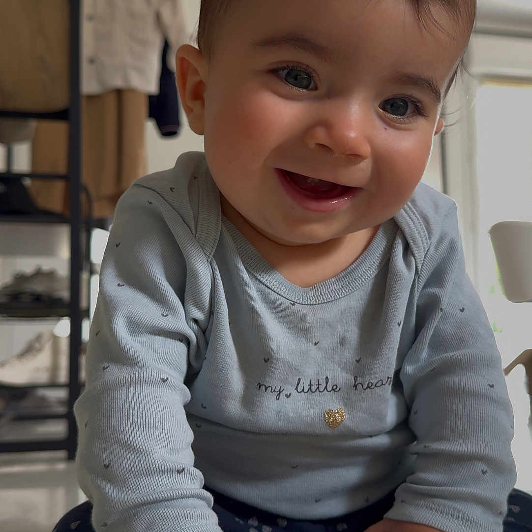 Lou a rejoint le concours — aidez-le/la à gagner de superbes lots ! baby, barefoot, child, clothing, cozy, cute, face, feet, floor, hands, happy, home, indoor, infant, long_sleeve_shirt, pants, playful, portrait, sitting, smiling