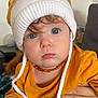 toddler, child, baby, blue_eyes, hat, knit_hat, orange, mustard_yellow, shirt, hand, curly_hair, face, indoor, person, portrait, closeup, couch, adult_hand, denim, expression
