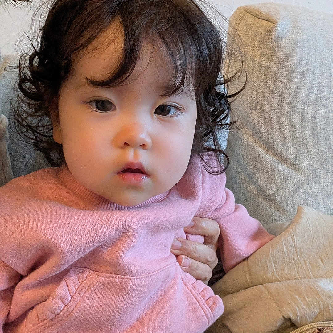 Mei joined the competition — help win amazing prizes! casual, child, clothing, comfortable, couch, cozy, curly_hair, cute, expression, face, hand, indoor, person, pink_sweater, portrait, seated, soft_lighting, toddler, warm, young_child