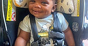 Milo is registered to the contest to win money with this photo: baby, car_seat, child, clothing, curly_hair, cushion, dark_skin, face, happy, harness, head, indoors, infant, photography, portrait, safety_buckle, seated, smiling, snoopy_shirt, vehicle