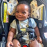 Milo is registered to the contest to win money with this photo: baby, infant, child, smiling, portrait, car_seat, harness, safety_buckle, seated, indoors, vehicle, snoopy_shirt, clothing, cushion, head, face, dark_skin, curly_hair, happy, photography