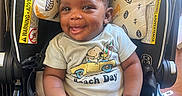 Milo joined the competition — help win amazing prizes! baby, infant, child, smiling, sitting, car_seat, safety_harness, onesie, snoopy, cartoon, portrait, indoor, wood_floor, happy, face, hands, feet, curly_hair, black_baby, high_chair